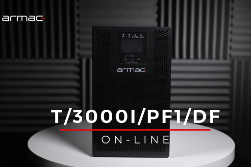 Czarny zasilacz awaryjny UPS stojący na białym okrągłym stoliku na tle ciemnych paneli akustycznych.