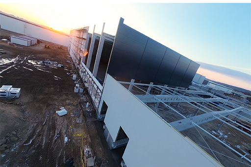 Lot dronem FPV po terenie budowy biura i magazynu popołudniem o zachodzie słońca.