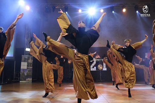 Kobiety i mężczyźni w formacji tanecznej na scenie ze światłami.